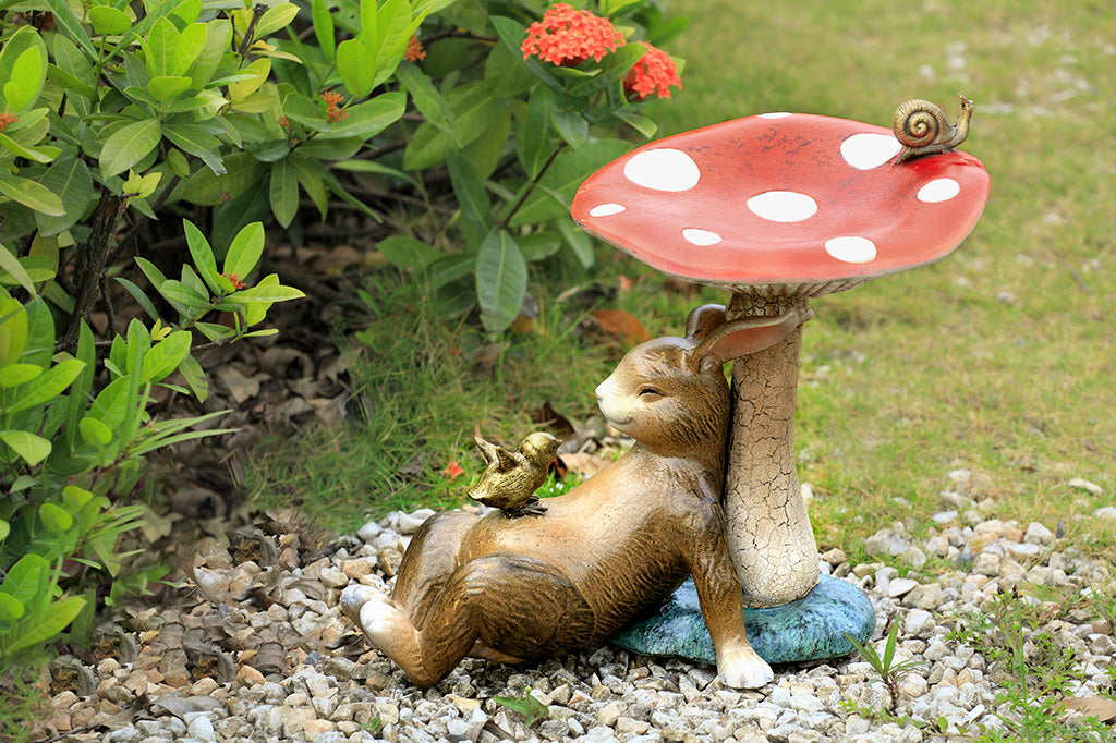 Bunny under a toadstool sculpture with chick and snail - mushroom is birdbath/birdfeeder, shown in garden