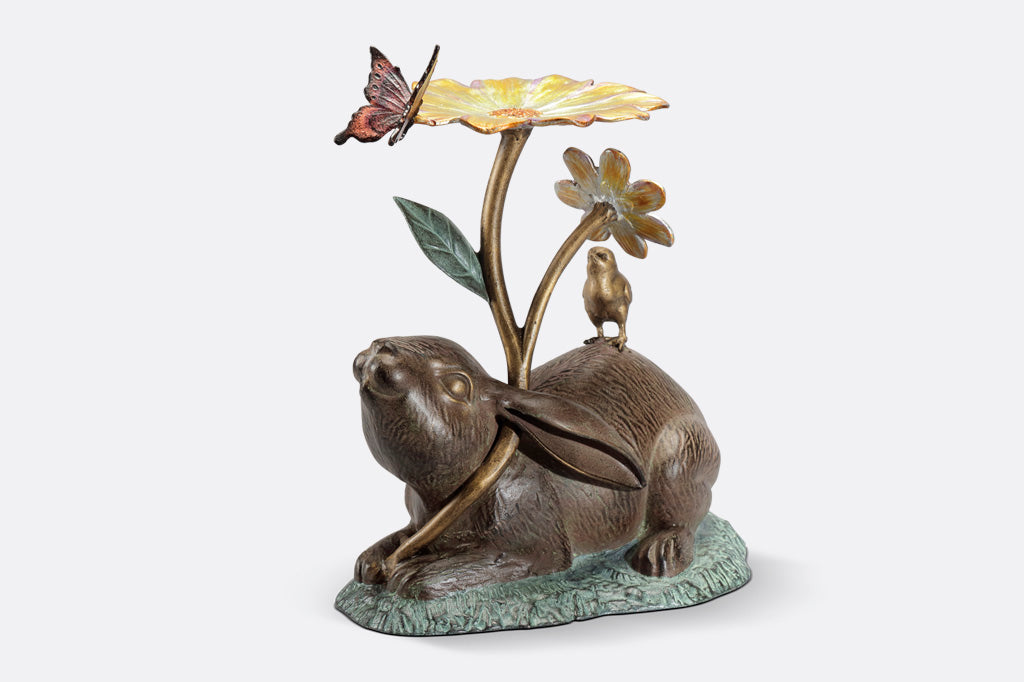 rabbit sculpture and birdbath/birdfeeder. A rabbit holds a blossom, surrounded by a chick, butterfly, and caterpillar