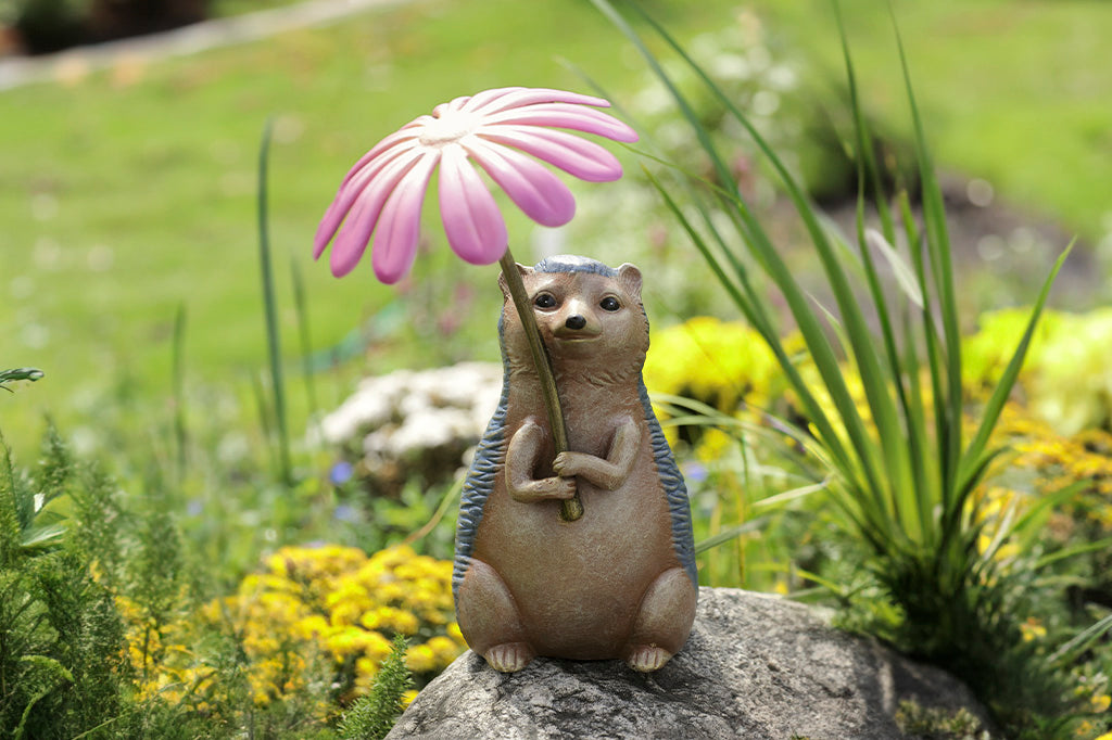 Garden sculpture of hedgehog holding flower blossom like an umbrella - shown in flower garden