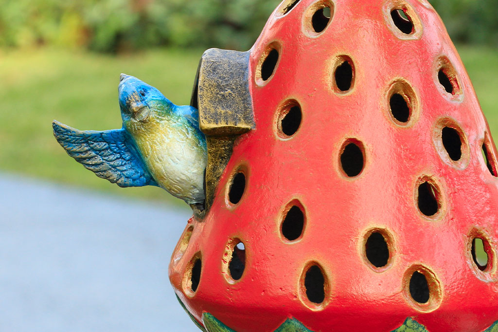 Red strawberry-shaped birdhouse with a decorative bird on a blurred natural background