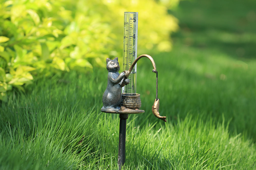 cast metal rain catcher with design of cat fishing with a basket holding the glass gauge