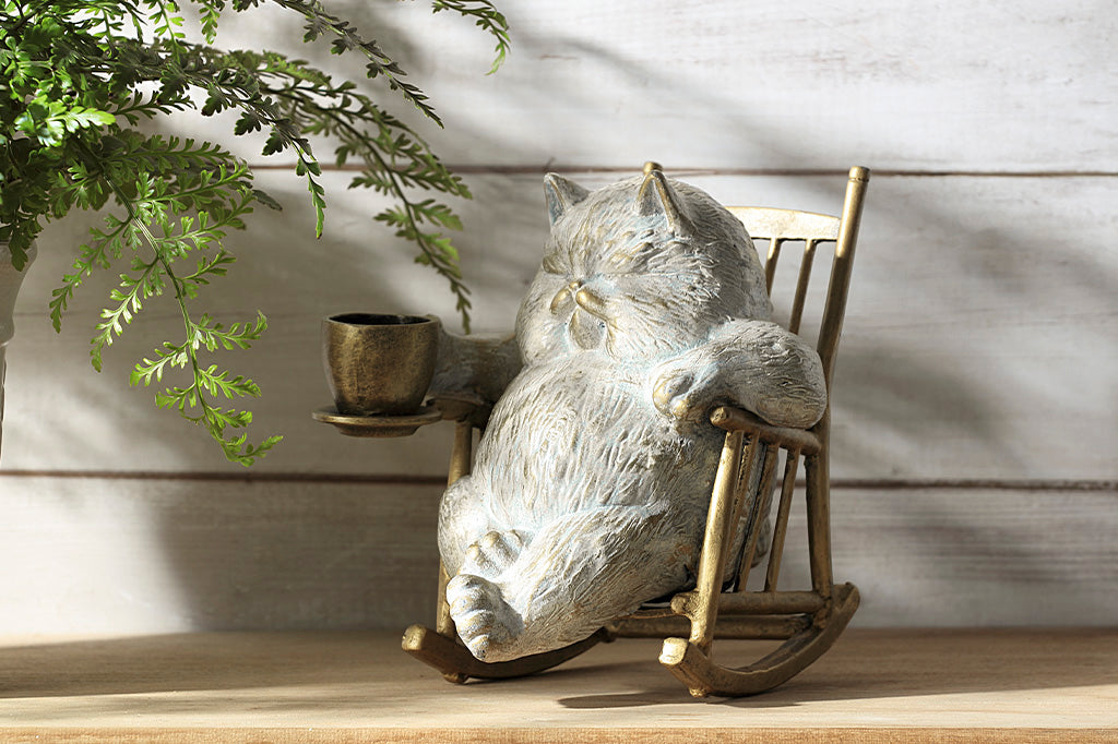 White cat in a rocking chair sculpture. Cat is restfully sitting with eye closes, holding a teacup which could hold LED tealight.