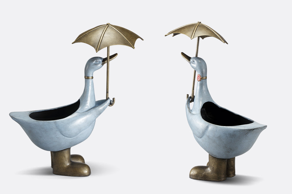 Alternate views of Slate blue goose planter shown holding an umbrella; she wears a flower choker,and rain boots.