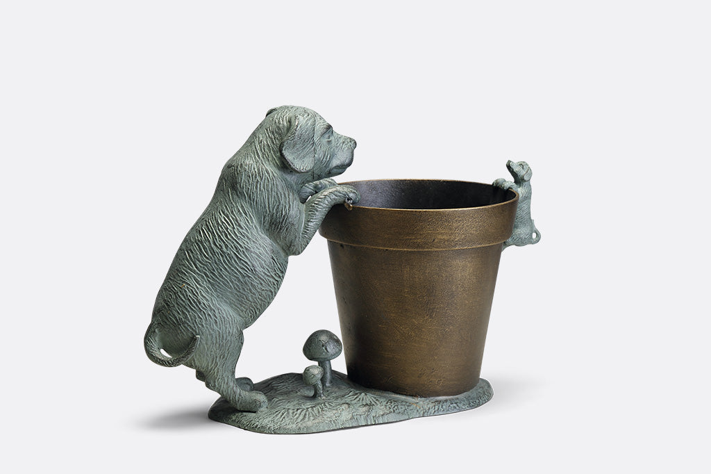 A planter statue with a small puppy holding onto the lip of the pot while a bigger dog peers over.