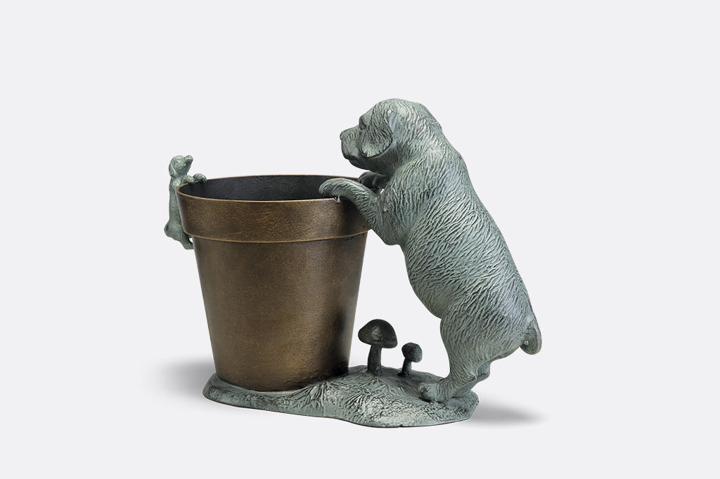 A planter statue with a small puppy holding onto the lip of the pot while a bigger dog peers over.