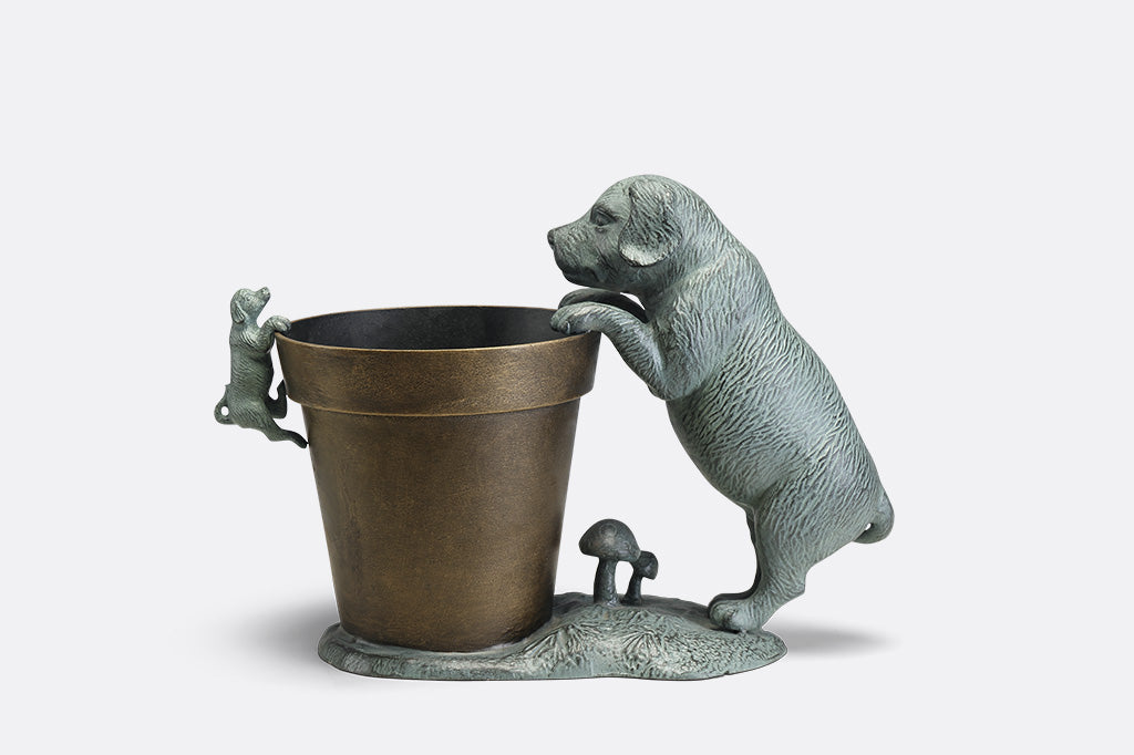 A planter statue with a small puppy holding onto the lip of the pot while a bigger dog peers over.