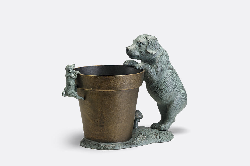 A planter statue with a small puppy holding onto the lip of the pot while a bigger dog peers over.