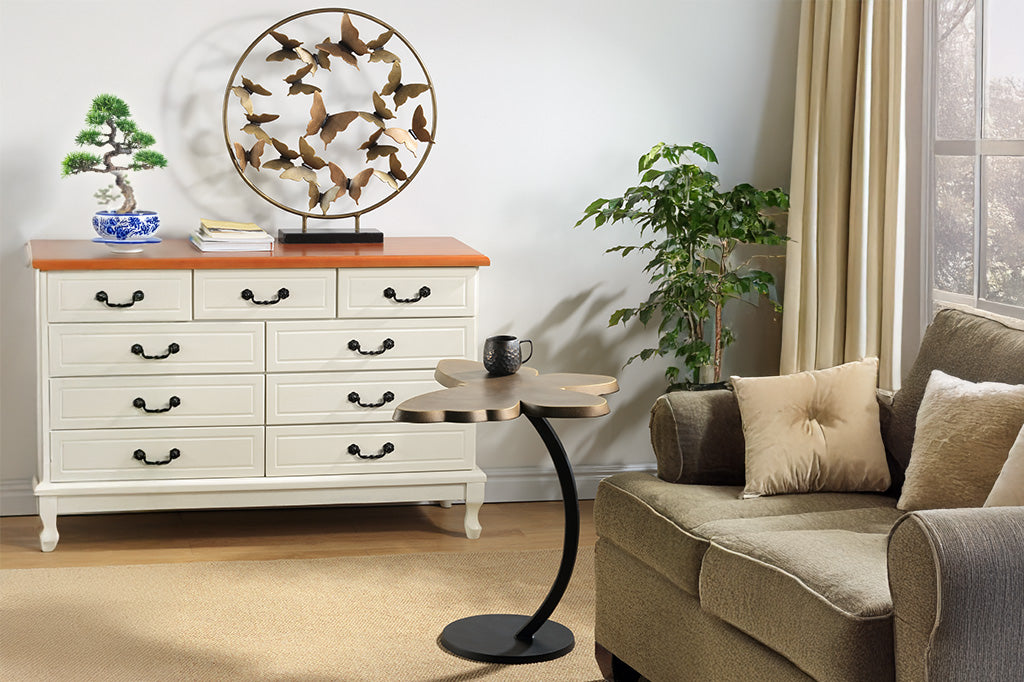 In a beige living room, by a couch is an accent table with a striking bronze butterfly silhouette as a tabletop. On top is placed a book and Moscow Mule cocktail cup.