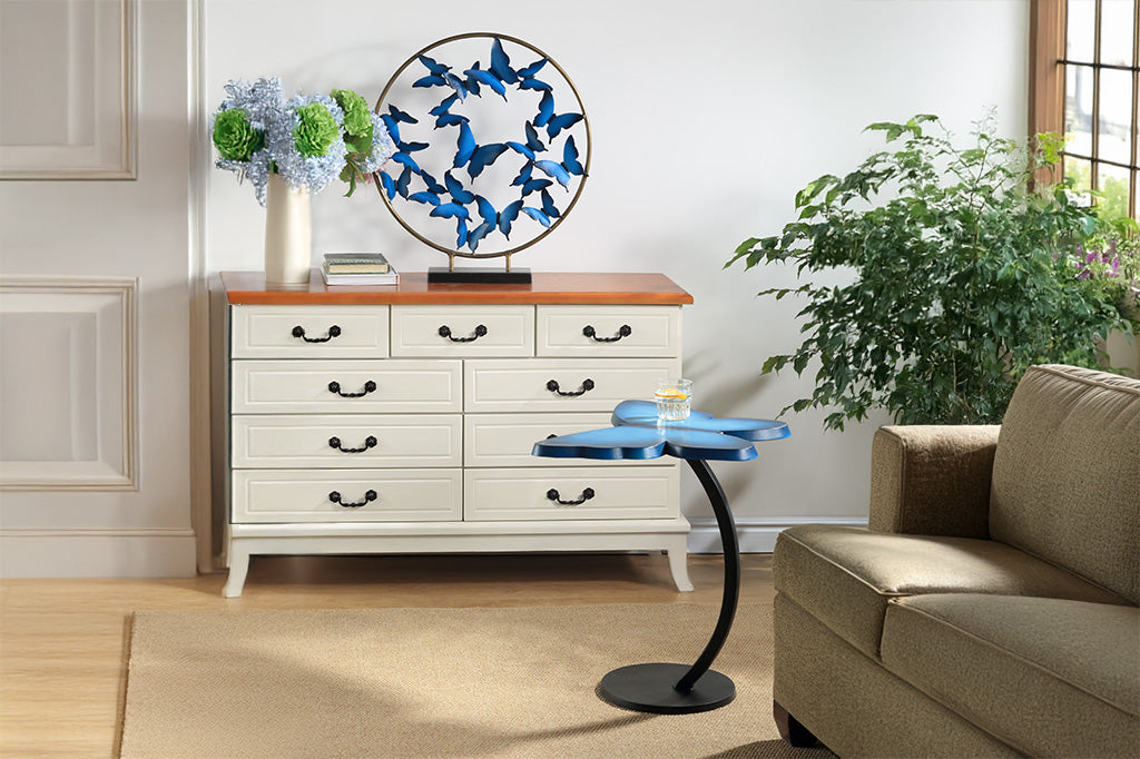 The Butterfly Accent Table in blue has a vibrant blue tabletop shown in a living room with tan furniture. Shown with lemon water in a glass on top.