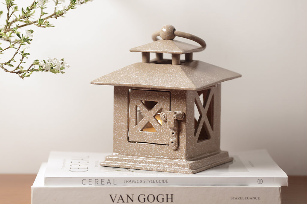cast metal lantern in tan with white speckles placed on stack of books #color_sand