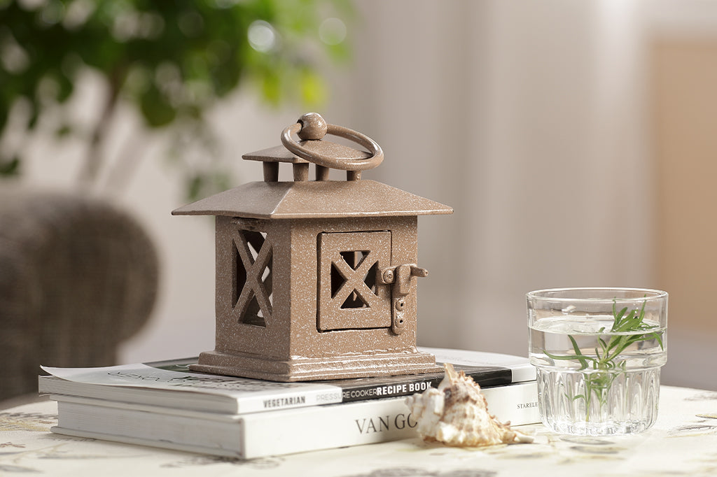 cast metal lantern in sand placed on stacked books next to water glass on marble counter #color_sand