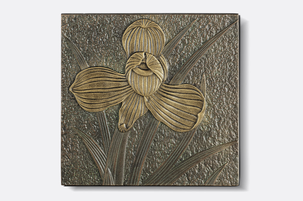 cast metal orchid stepping stone, blooming four petaled orchid. orchid bloom amongst foliage.
