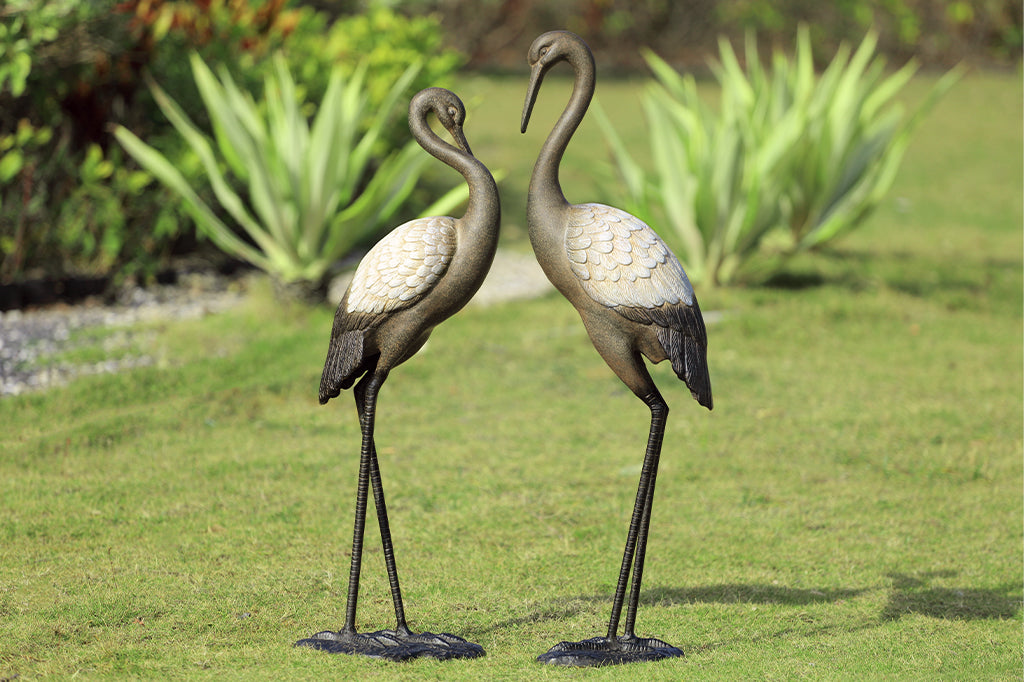 cast metal pair of two garden crane sculptures with white wings and brown bodies set in garden setting