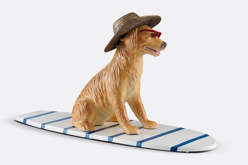 cast metal dog sculpture sat on stripped white and blue surfboard face right. See dogs floppy ears and texture of cast metal straw hat