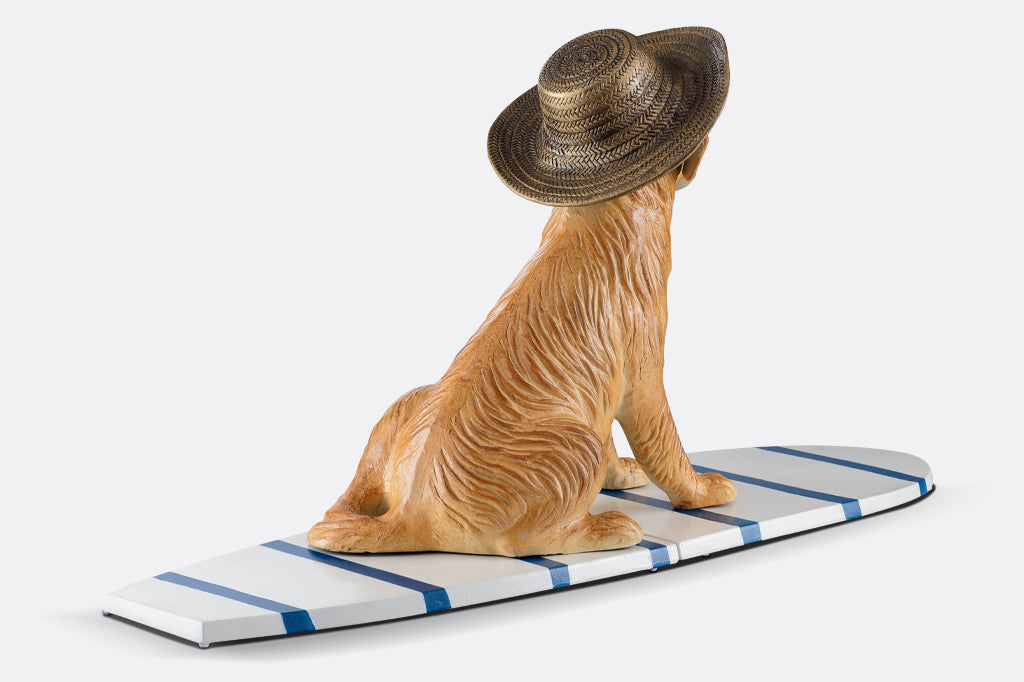 cast metal dog sculpture sat on stripped white and blue surfboard face back. See dogs floppy ears and texture of cast metal straw hat