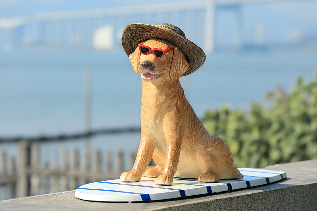 cast metal dog with sunglasses sat on stripped blue and white surfboard set in urban beach scene