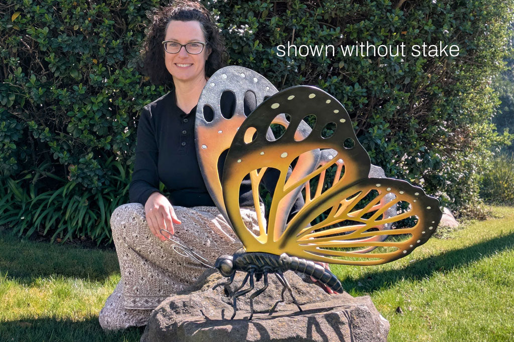 Person holding a large butterfly sculpture outdoors with text 'shown without stake'.
