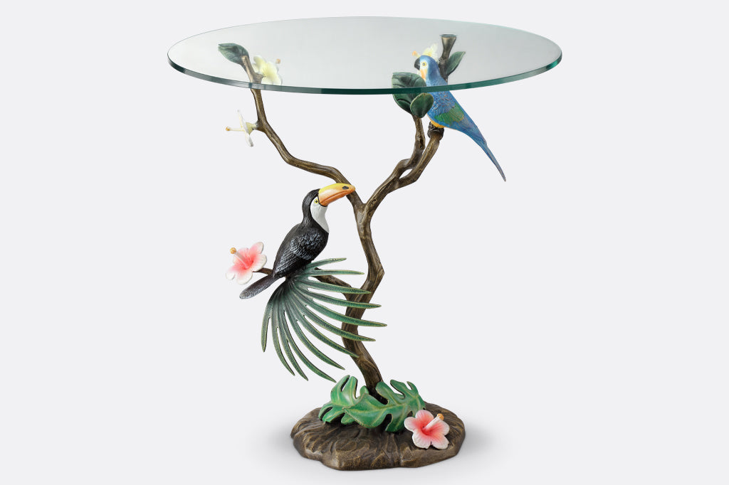 cast metal toucan and parrot perched on branch table with glass top
