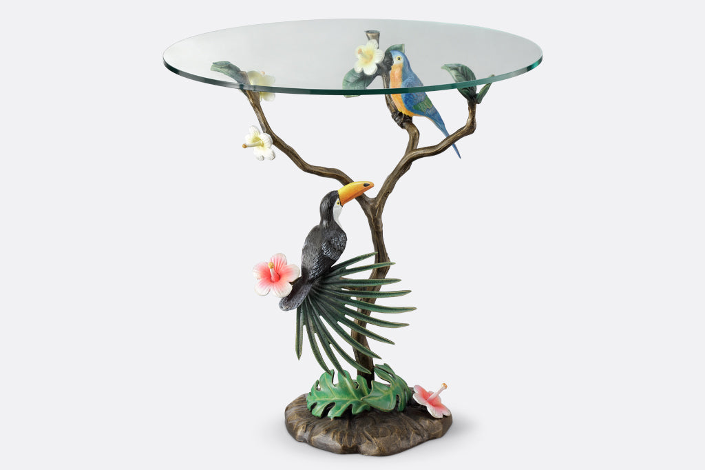 cast metal toucan and parrot perched on branch table with glass top