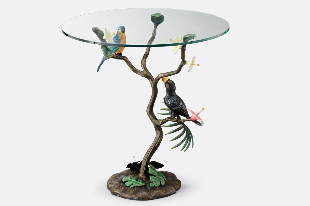 cast metal toucan and parrot perched on branch table with glass top
