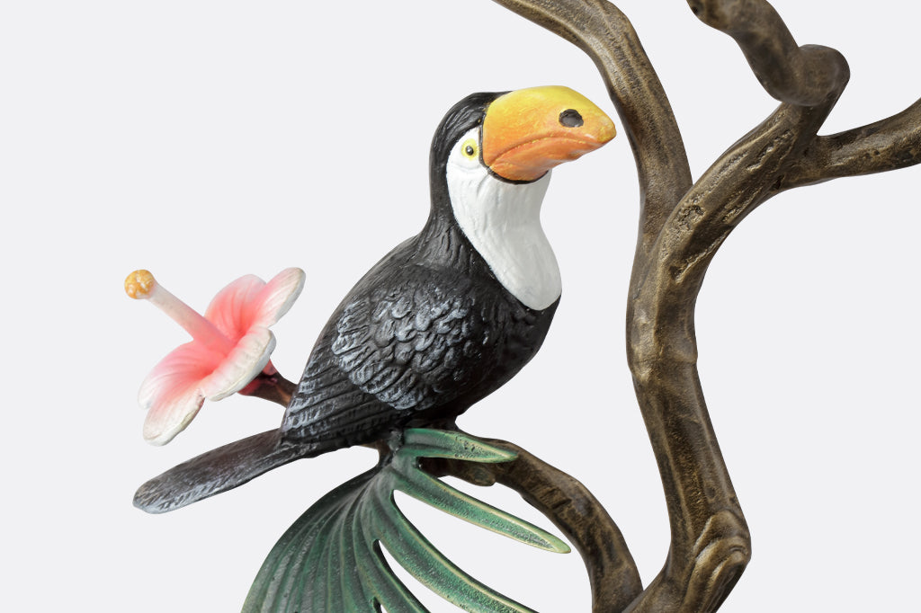 detail view of black and white toucan perched on branch with hibiscus bloom