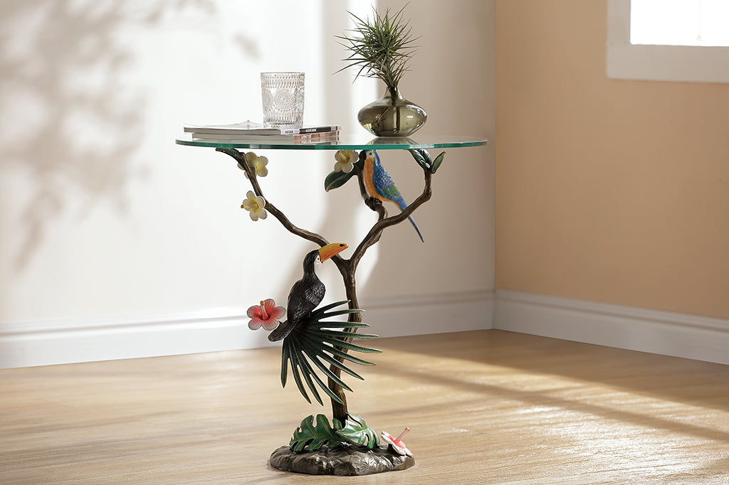 cast metal table featuring a branch with a toucan and parrot along with hibiscus blossoms with a glass top set in living room scene