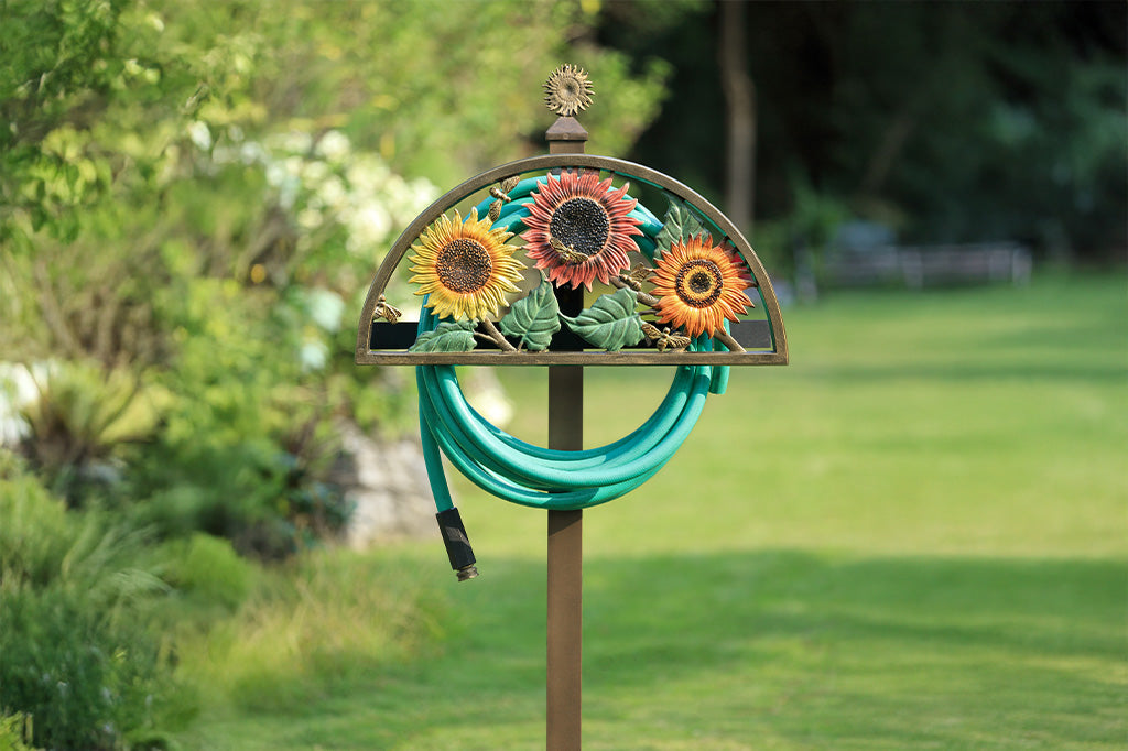 Decorative garden hose holder with sunflower design in a garden setting