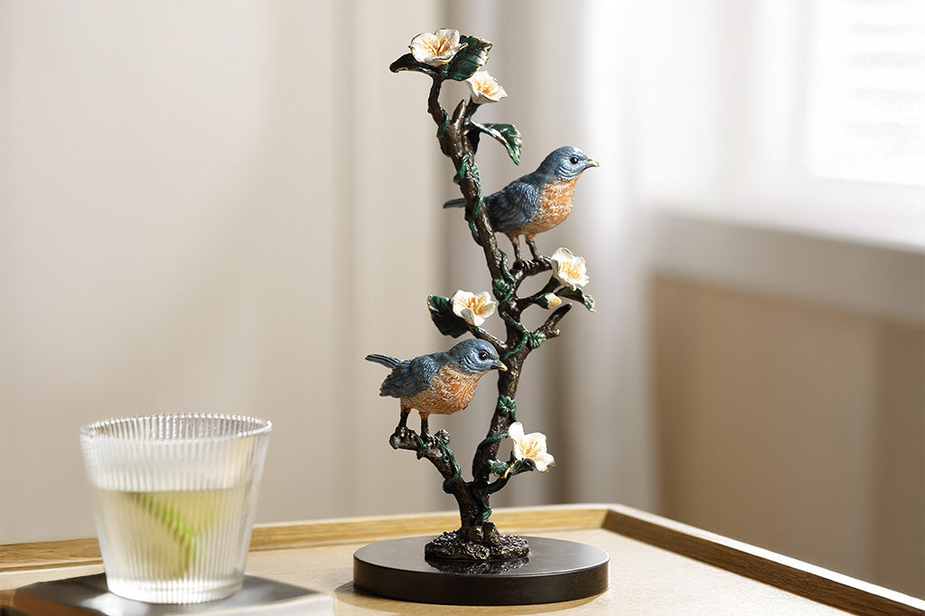 Decorative sculpture of birds on a branch with flowers on a table.