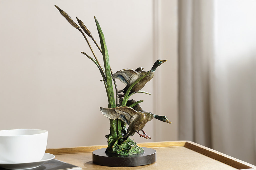 Brass sculpture of two ducks on a stand with reeds on a white background