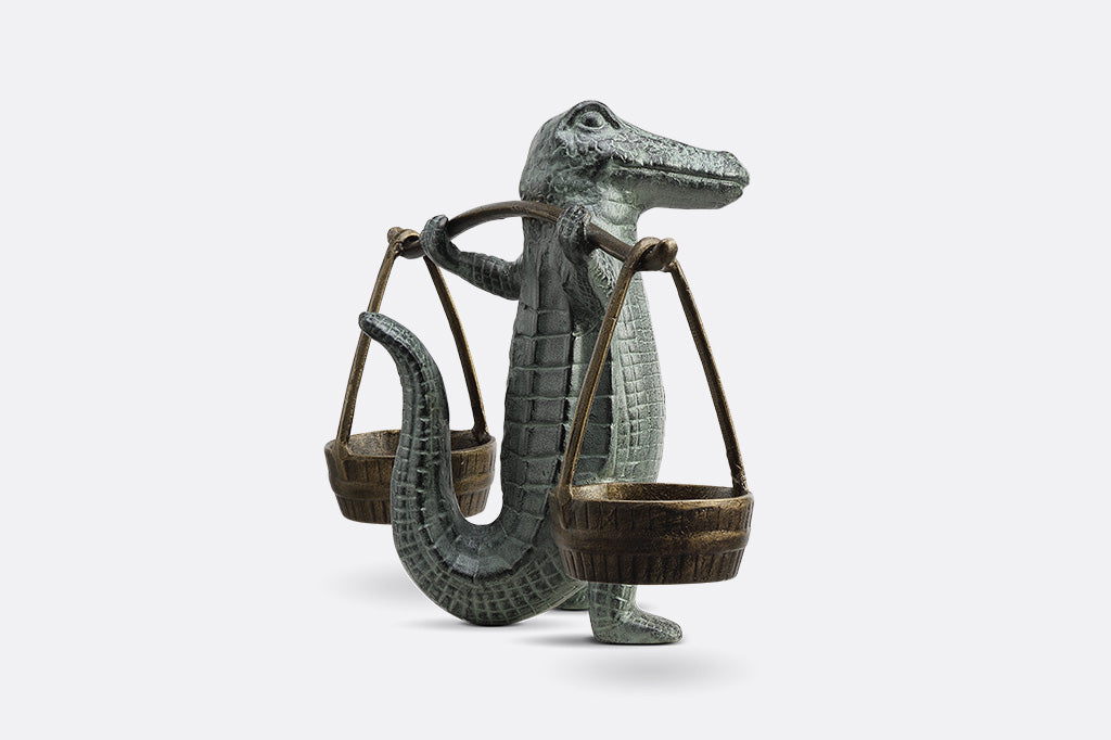 A sculpture of an alligator holding up two buckets.
