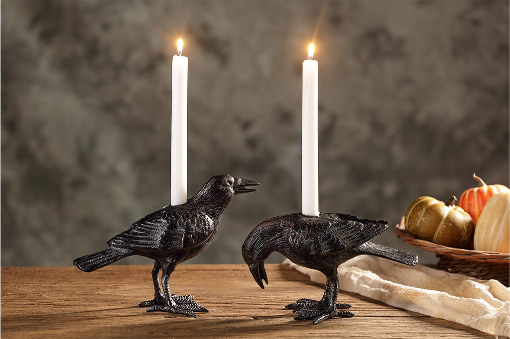 Two black crow candle holders with lit white candles on a wooden surface.