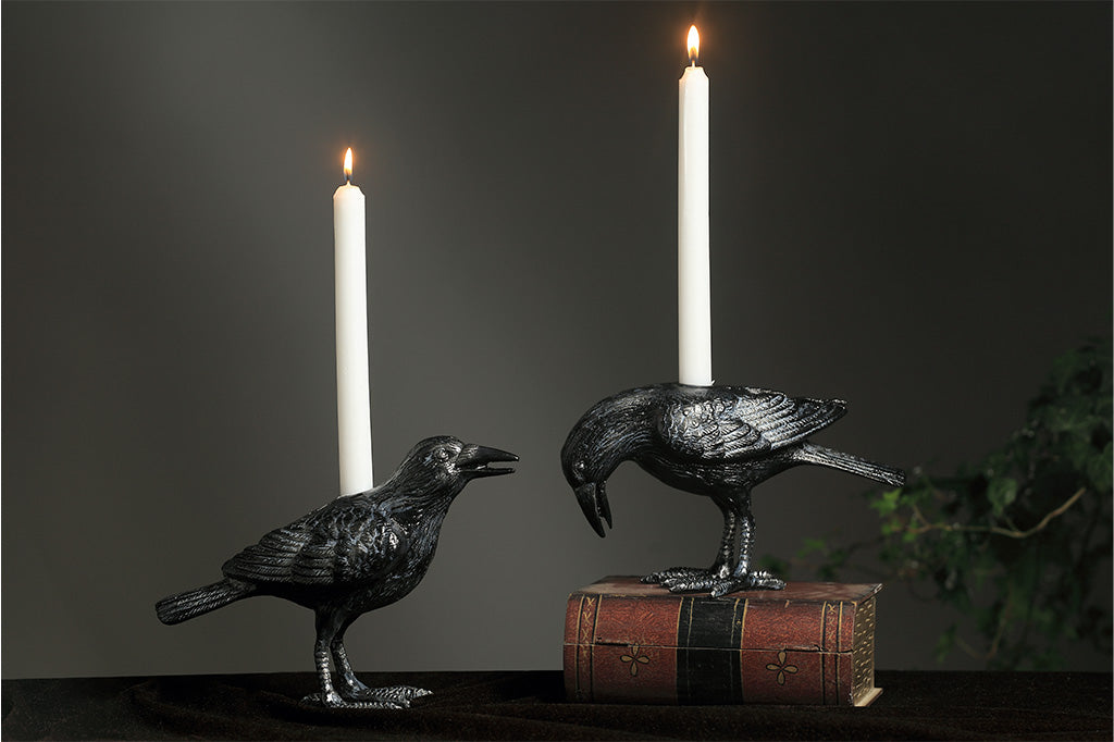 Two metal crow candle holders with candles on a dark background