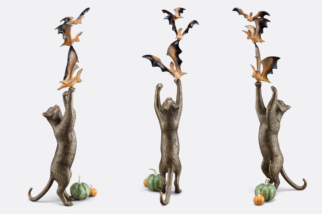 multiple views of cast metal cat sculpture on back paw reaching/ playing with orange and black bats with two pumpkins by base of kitty hind paws. Face right left and back