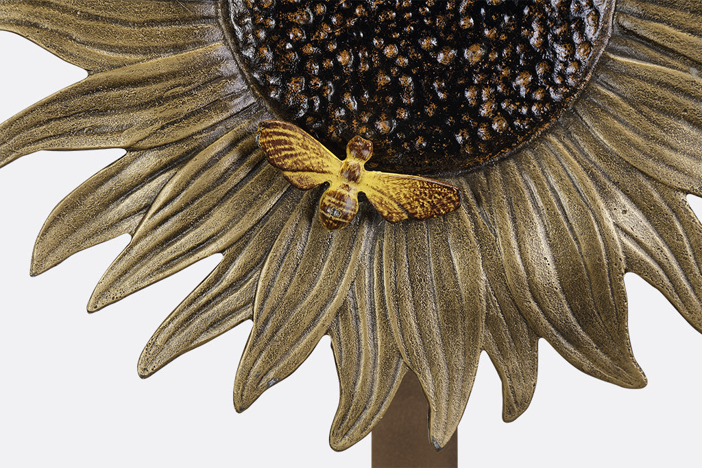 A garden stake hose holder with a sculpture of a sunflower and bird.