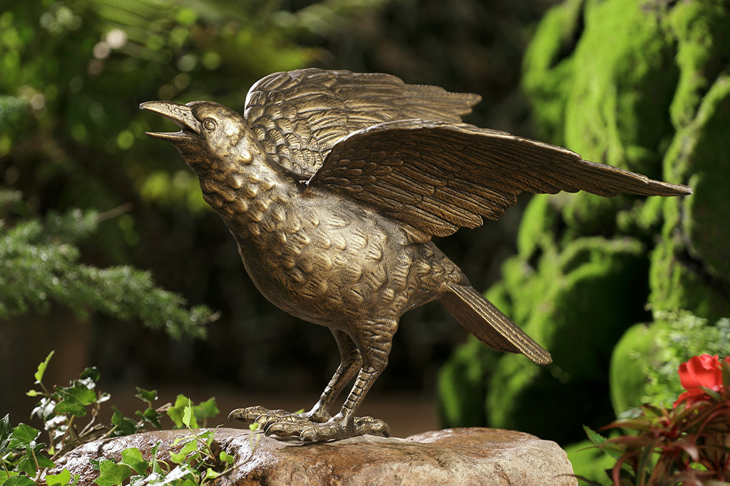cast metal crow sculpture face left perched on rock set in garden scene