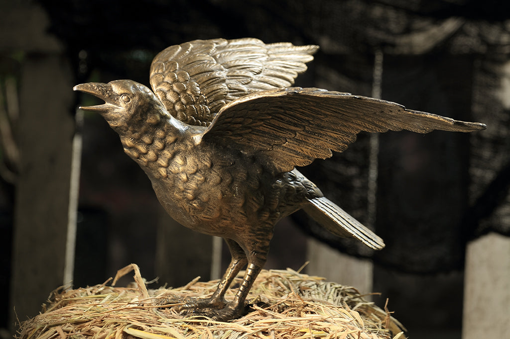 cast metal crow sculpture perched on hay bail