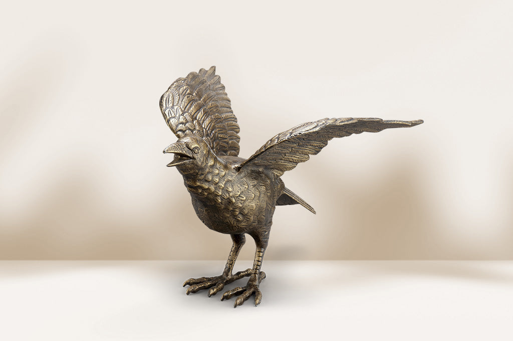 Bronze cast metal sculpture of a crow with open wings on a beige background