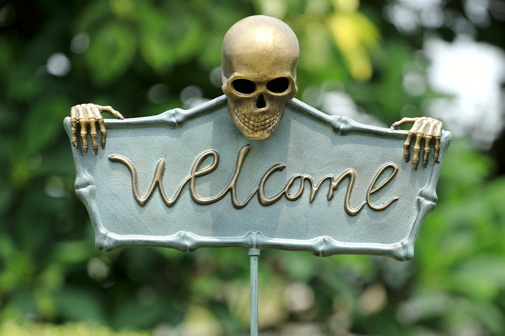 cast metal welcome sign with skeleton holding sign set in garden setting