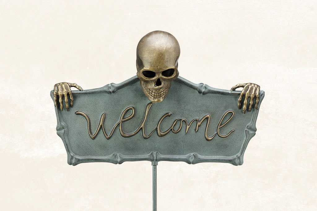 cast metal welcome sign with skeleton holding sign set in garden setting