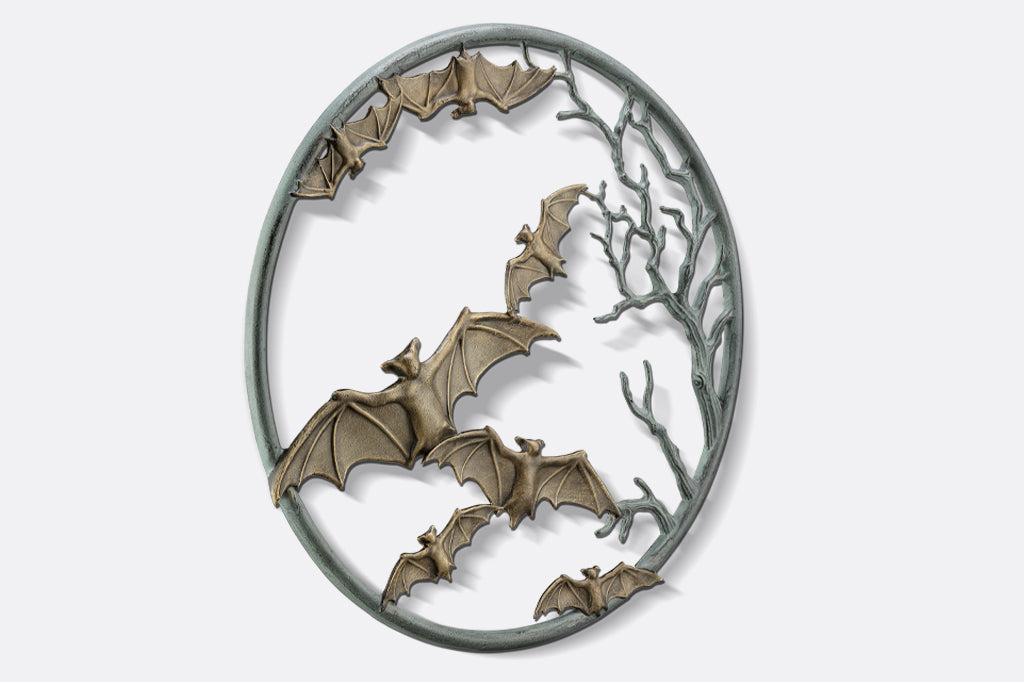 cast metal circular wall plaque featuring flying bats and spooky branches side view