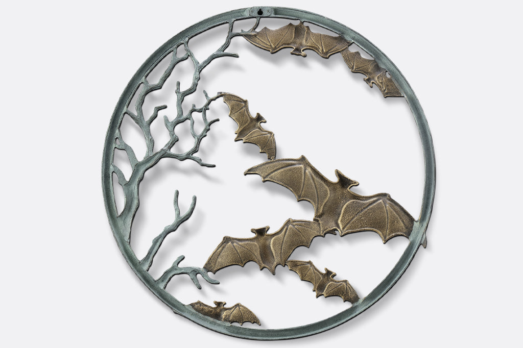 Back view of cast metal circular wall plaque featuring flying bats and spooky branches back view, mounting hardware shown