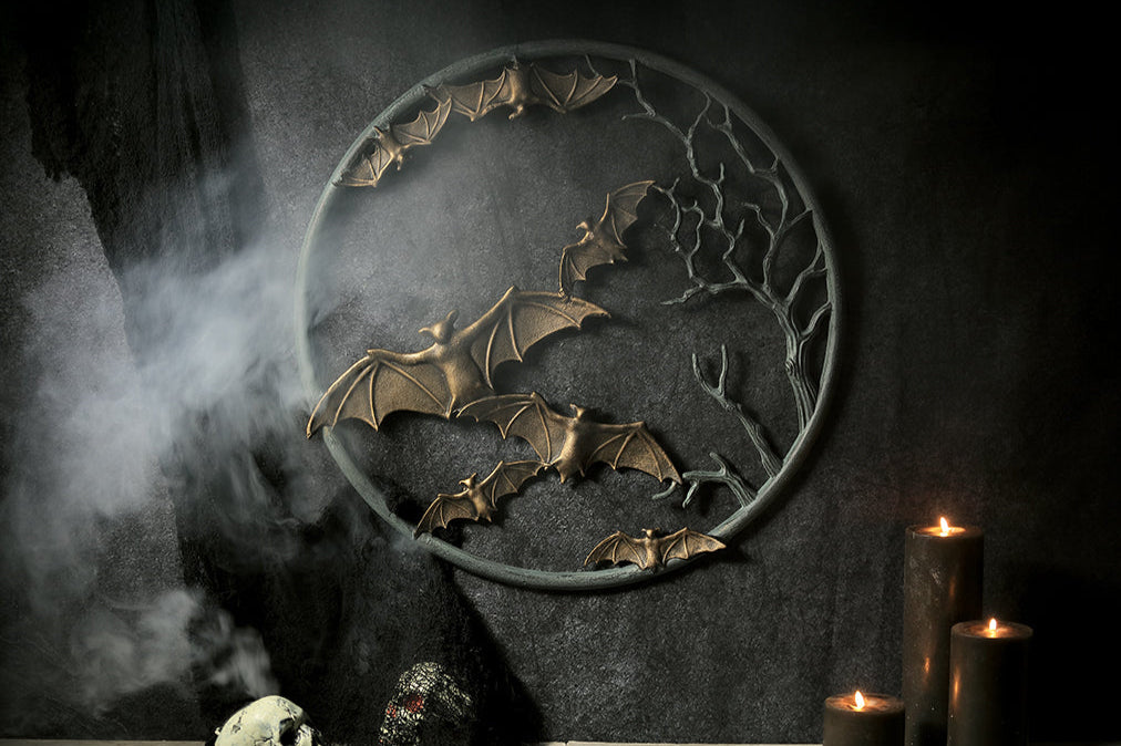 cast metal circular wall plaque featuring flying bats and spooky branches set on dark wall