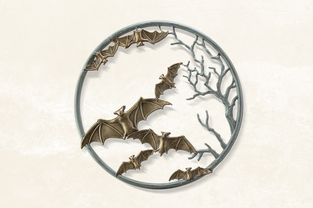 cast metal circular wall plaque featuring flying bats and spooky branches set on light color wall