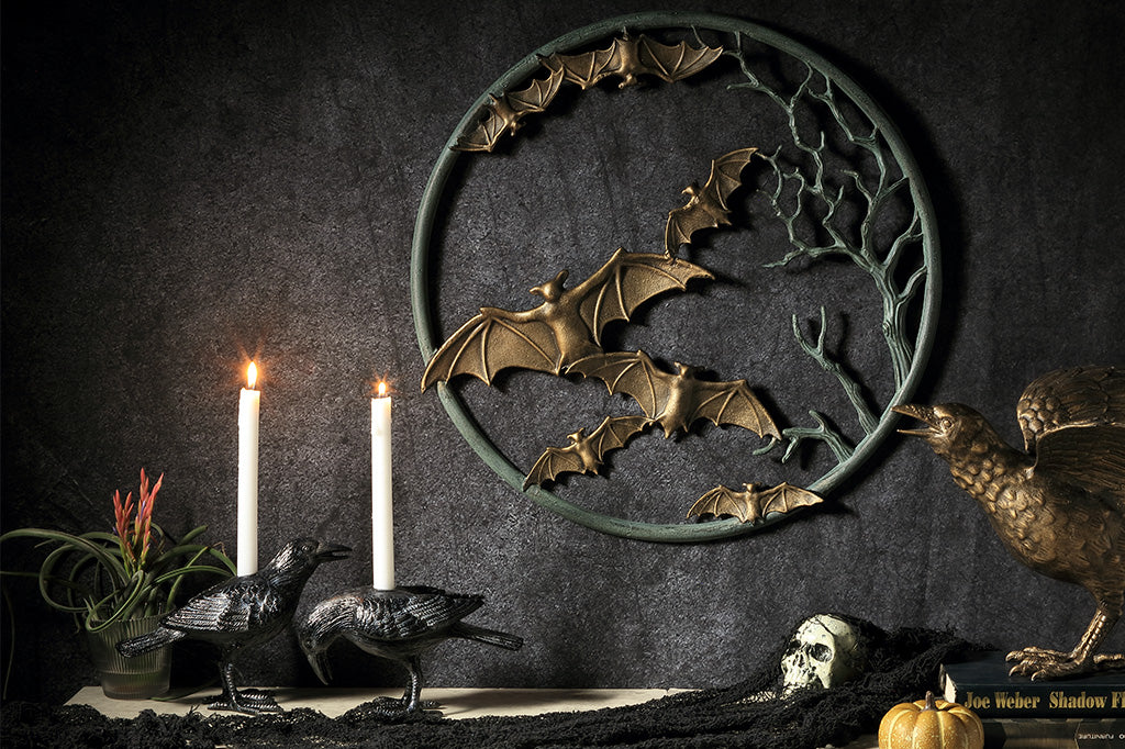 Decorative wall art with bats, candles, raven candleholders, and a crow on a dark background in Halloween scene