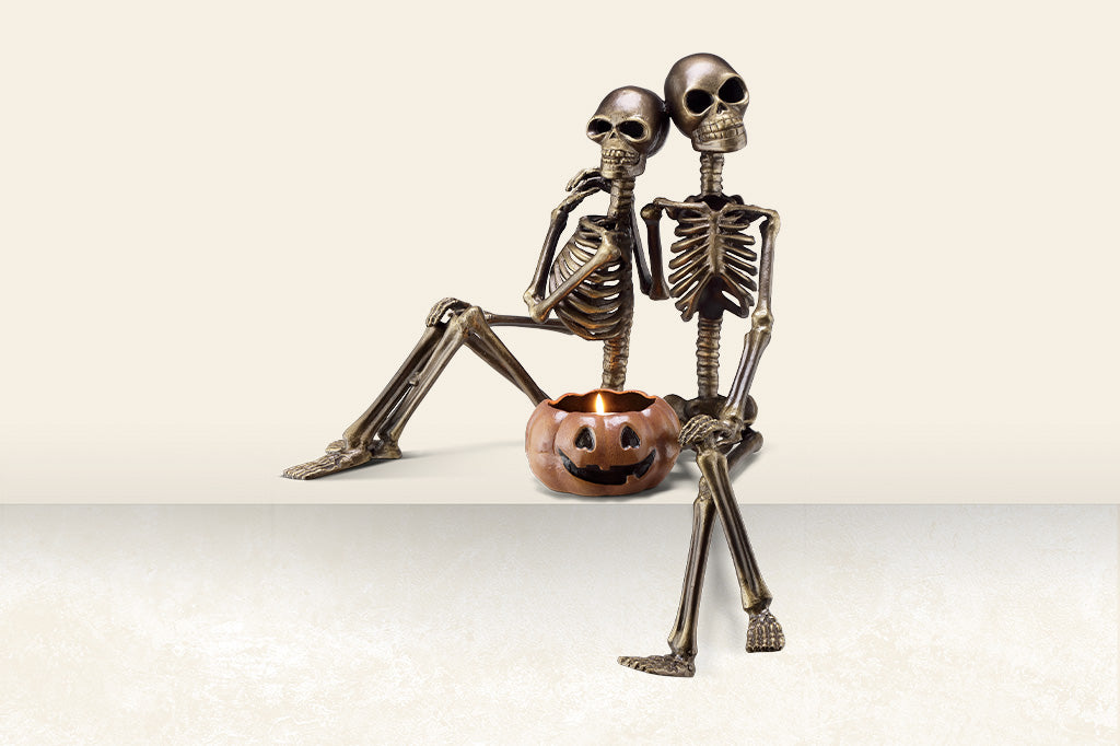 Decorative skeleton couple with a pumpkin seated on ledge, cast metal Halloween sculpture