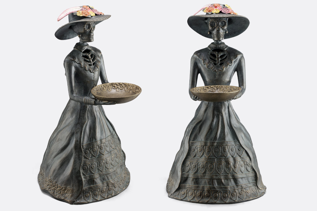 side and front on view of la catrina cast metal sculpture, skeleton figure in dress and hat holding decorative bowl
