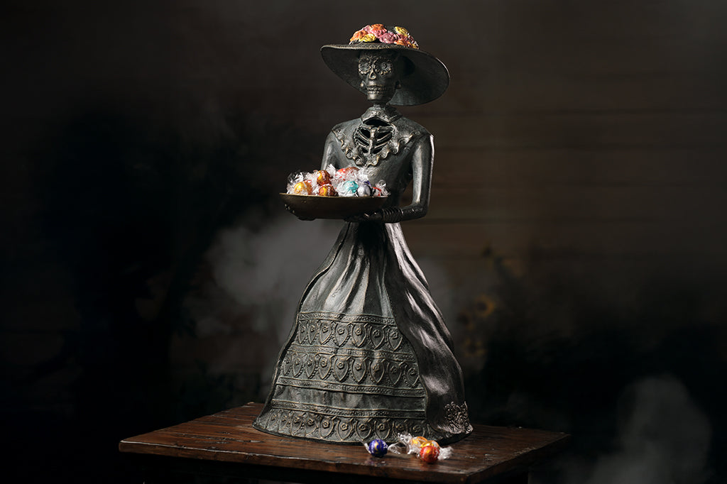 cast metal sculpture of la catrina with decorative bowl holding candies