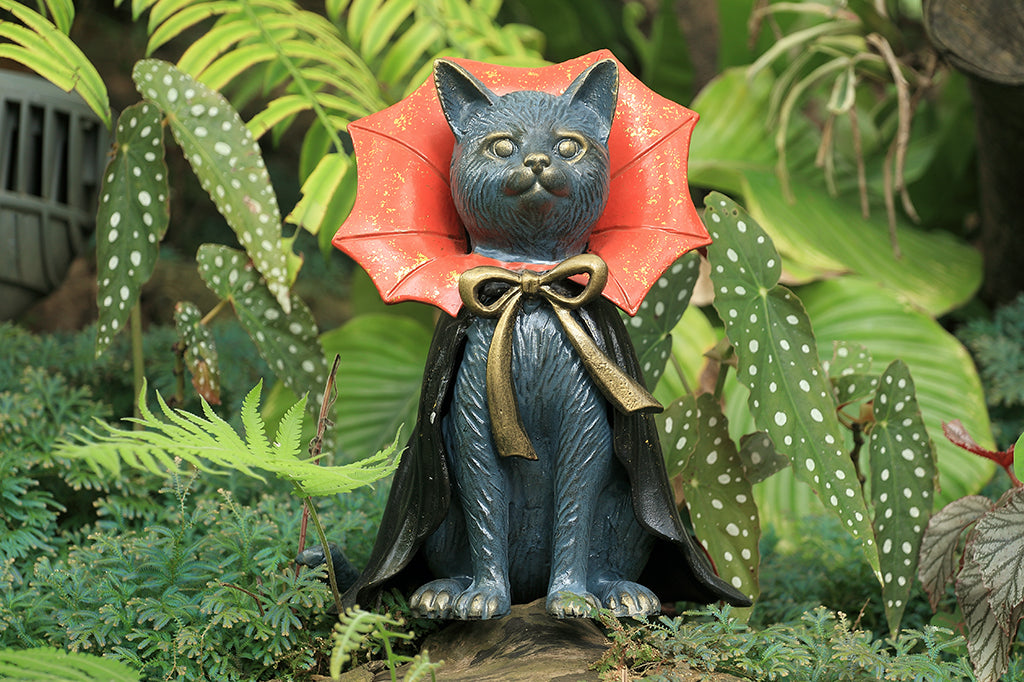 cast metal cat with red and black cape set in garden scene