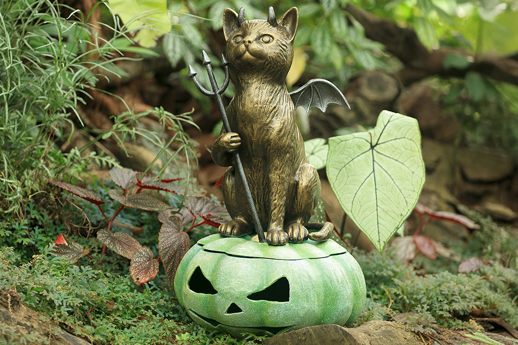 cast metal devil cat with wings sat on green jack o lantern set in garden scene