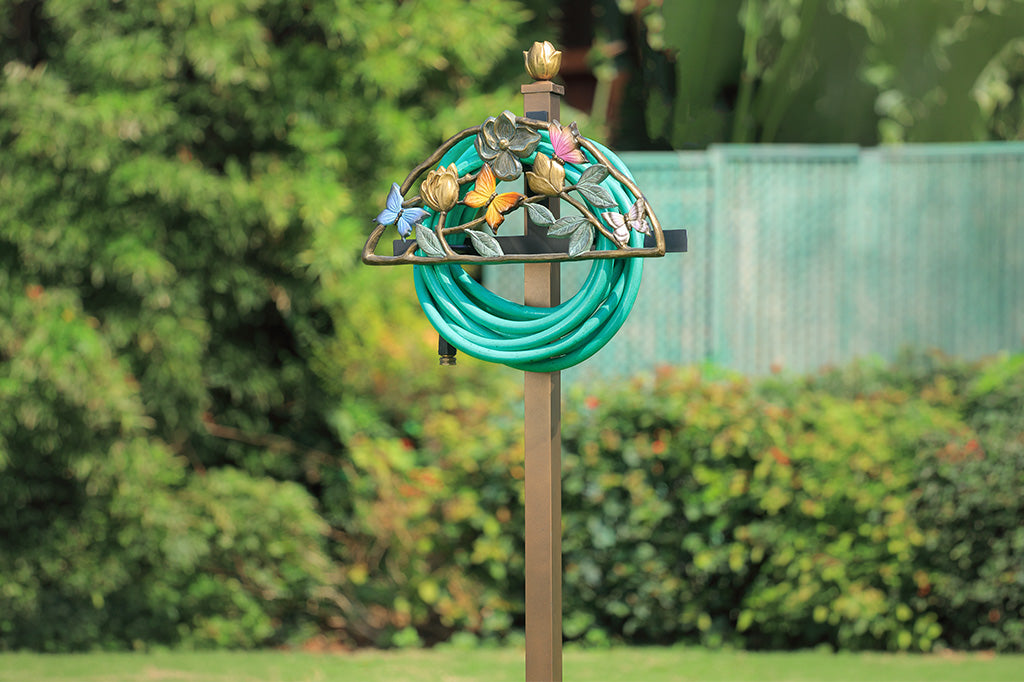 Decorative garden hose holder with floral design against a blurred green outdoor background